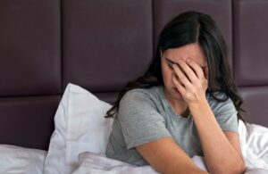 Depressed and sad Young woman sitting in bed, holding hand over face.