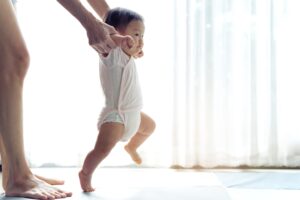 Happy little baby learning to walk with mother help at home. Baby growth and development