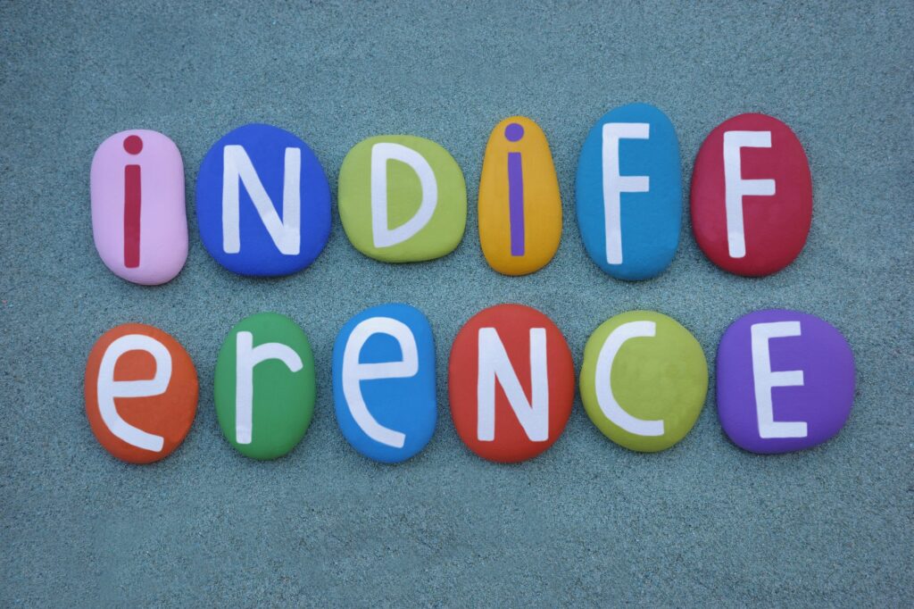 Indifference word composed with multi colored stone letters over green sand