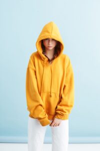 Young beautiful girl with two braids in orange hoodie and white jeans thoughtfully looking in camera