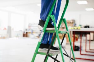 Worker climbing green ladder in factory workshop